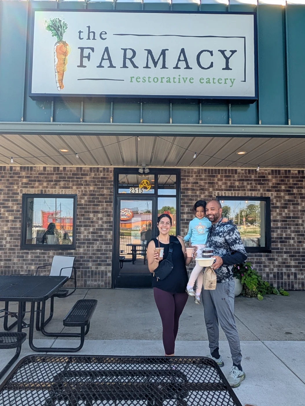 Kim and her family holding drinks and takeout outside The Farmacy restorative eatery, beneath its sign.